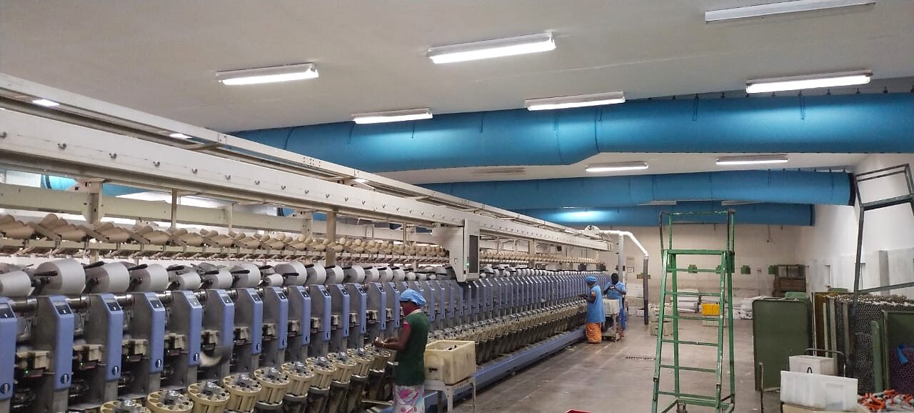 Blue fabric air ducts running the length of a spinning mill, distributing cooled air over rows of machines