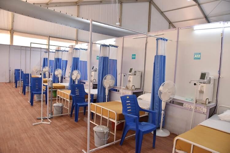 Rows of beds with blue curtains and pedestal fans in the airport COVID-care facility ventilated by TurboaSOX